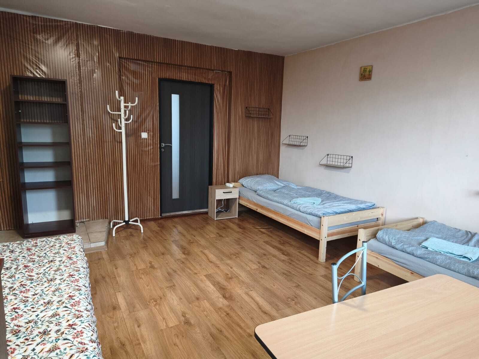 Een kamer met houten vloer, een bed, een klein tafeltje, een kapstok en een kledingkast.