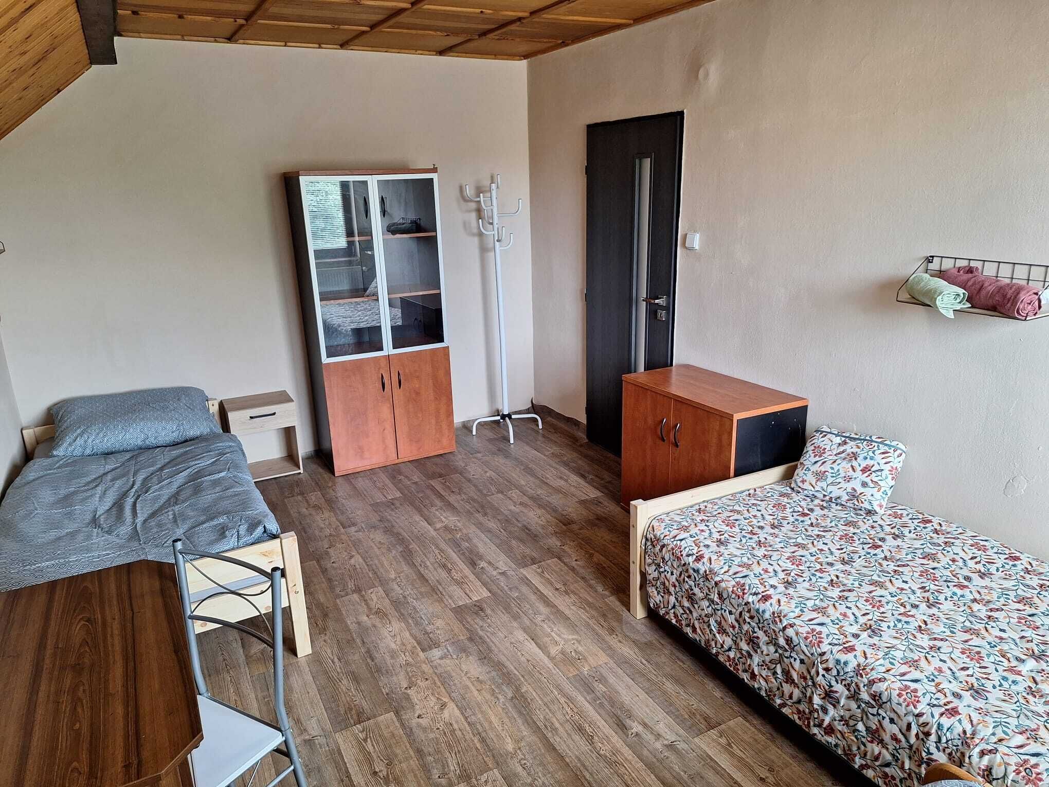 A compact room with two beds, a wardrobe, a desk, and a chair.