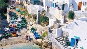 A coastal village with white buildings, a clear blue sea, and boats docked along the shore.