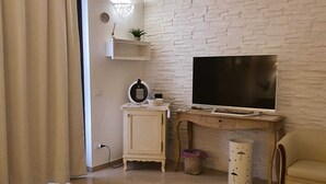 A living room with a TV, a small cabinet, a plant, and a trash bin.