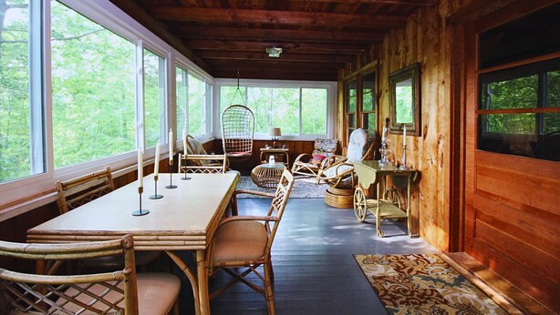 A cozy cabin interior with a wooden interior, large windows, a dining table, and wicker furniture. - Cozy, welcoming Berkshires cottage – perfect home base & place to unplug! (Stockbridge)