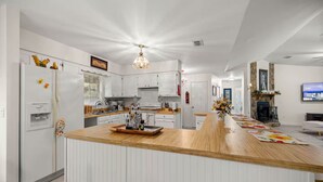 A modern kitchen with white cabinetry, a wooden island, and a stone fireplace. - Vintage Fall retreat Near Springs Cozy Fireplace
(Williston)