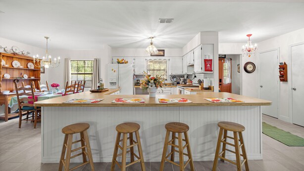 A spacious kitchen with a central island, wooden bar stools, and a dining area with chairs and a table. - Vintage Fall retreat Near Springs Cozy Fireplace
(Williston)
