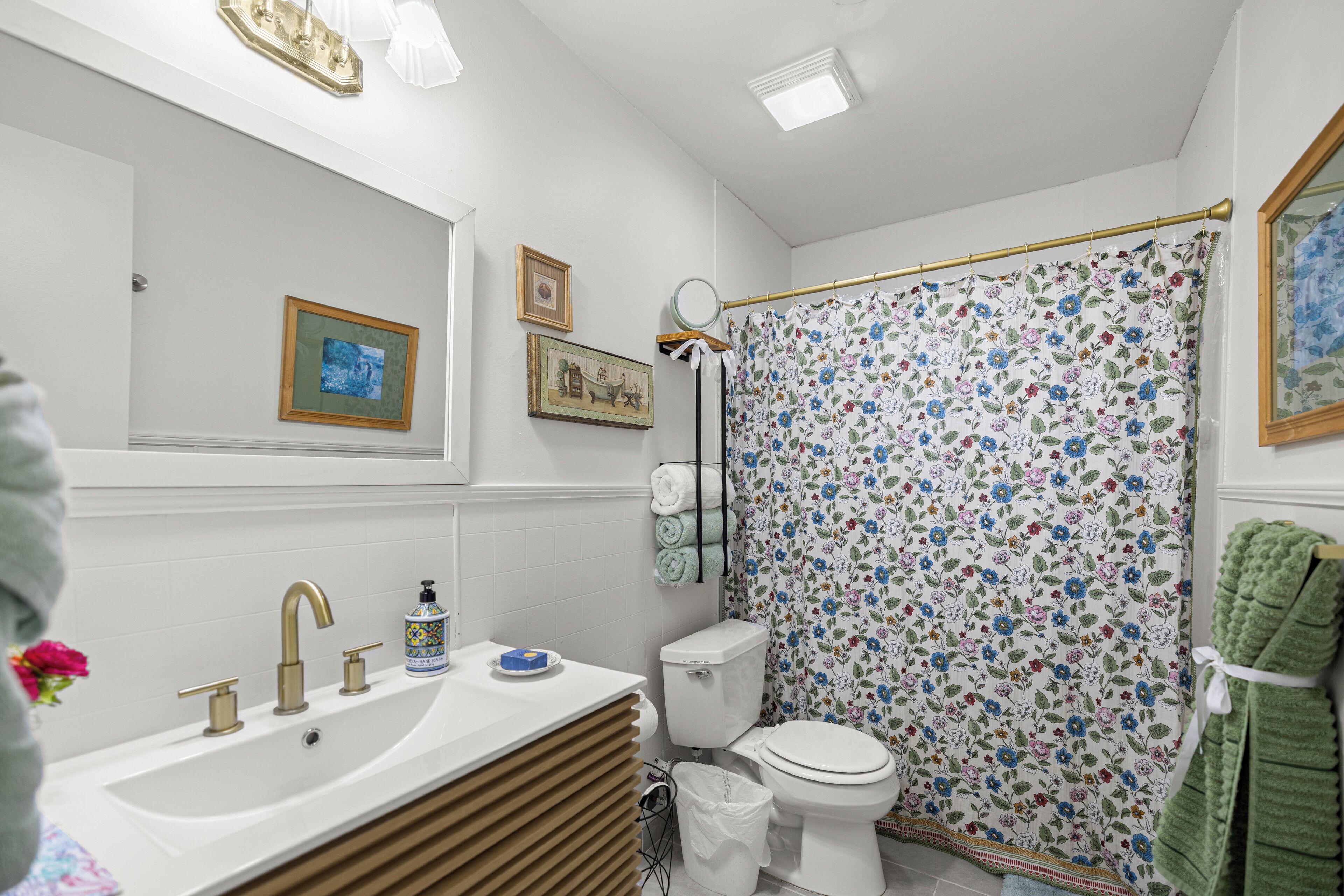 Ein Badezimmer mit einem weißen Waschbecken, goldenen Wasserhähnen, einer Toilette und einem Duschvorhang mit Blumenmuster.