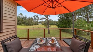 A covered patio with a table and chairs, a large orange umbrella, and a view of a grassy area with trees. - Vintage Fall retreat Near Springs Cozy Fireplace
(Williston)
