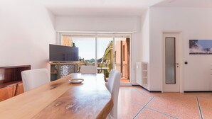 Een eetgedeelte met een houten tafel, stoelen, een televisie en uitzicht op buiten.