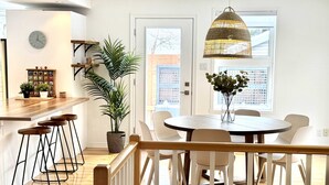 Eine moderne Küche mit einer Holzarbeitsplatte, Barhocker, einem Esstisch mit Stühlen, einer hängenden Pendelleuchte und einem Blumentopf.
