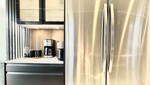 Uma cozinha moderna com geladeira de aço inoxidável, forno embutido e cafeteira no balcão.