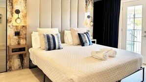 Quarto de hotel com uma cama grande, duas mesas de cabeceira, uma parede decorada em mármore e vista para o exterior por uma janela.