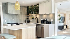 A modern kitchen with a central island, stainless steel appliances, and a hanging light fixture. - L Oasis Boheme Hot tub 2 Bedrooms | Free EVCharger (Boischatel)
