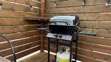 A barbecue grill with a gas tank, a metal cart, and a chair.