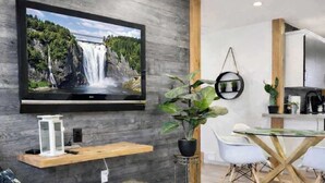 A modern kitchen with a TV mounted on a wooden wall, a dining table with chairs, and a potted plant. - 2 minutes from the falls | Private terrace | Sleeps 6 (Boischatel)