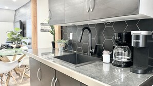 A modern kitchen with a black hexagonal backsplash, stainless steel cabinets, a black faucet, a Keurig coffee maker, and a glass jar on the counter. - 2 minutes from the falls | Private terrace | Sleeps 6 (Boischatel)