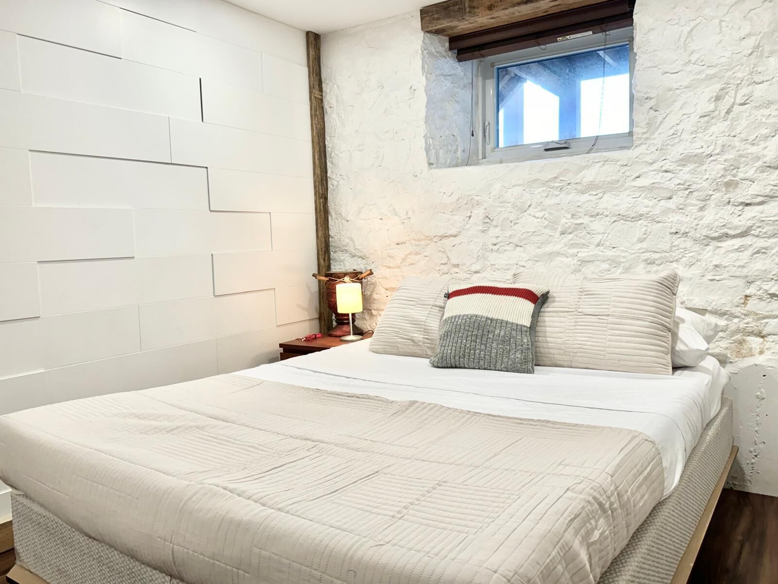 Un dormitorio con cama, mesita de noche con lámpara, ventana y pared con textura.