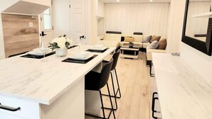 Une cuisine moderne avec un plan de travail en marbre, des chaises noires et un coin repas comprenant un canapé et une table basse.