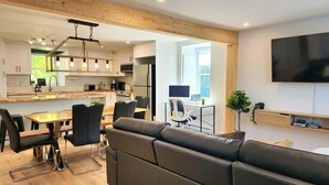 Una cocina moderna con vigas de madera, un comedor con sofá de cuero negro y un televisor de pantalla plana montado en la pared.