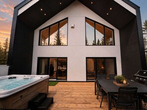 A modern two-story house with a hot tub, dining area, and outdoor grill.