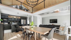 Una cocina moderna con armarios oscuros, una mesa de comedor de madera y un televisor montado en la pared.