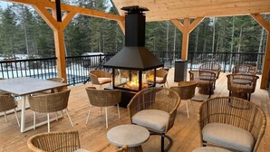 Un patio exterior con mobiliario de mimbre, un hogar para fuego y vistas a un bosque nevado.