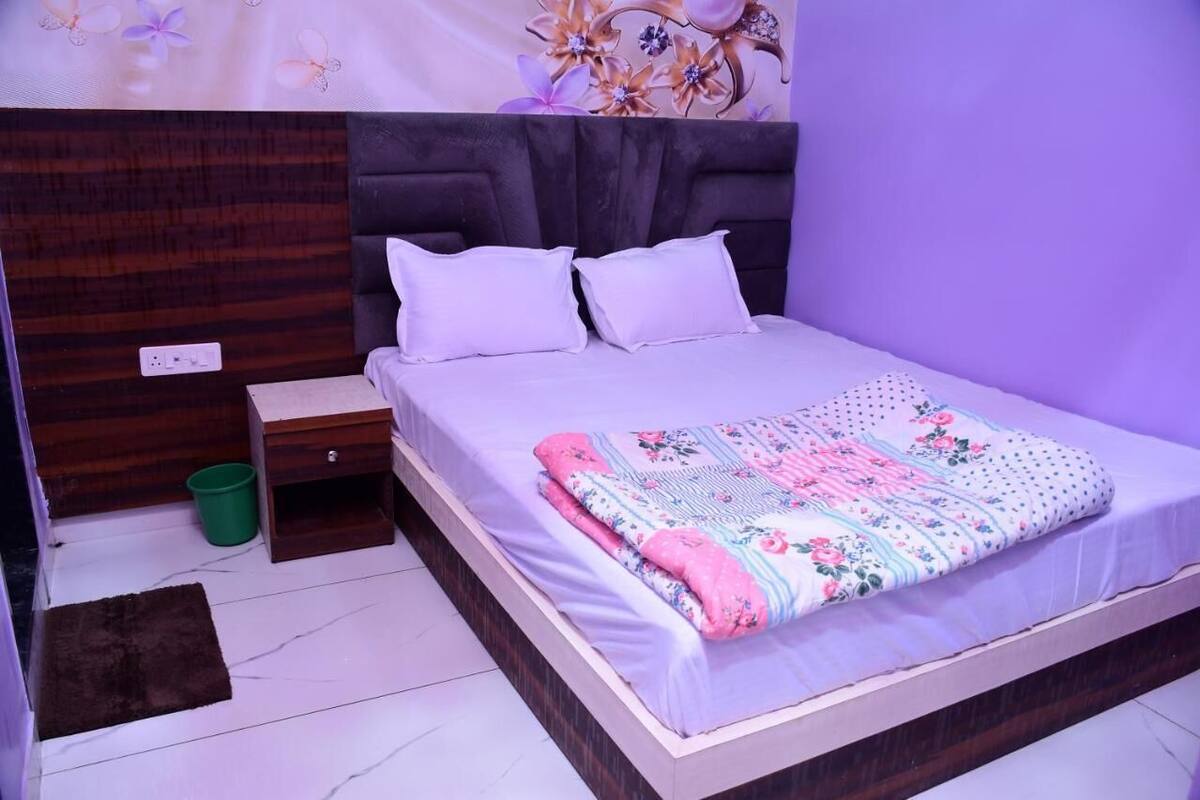 A bedroom with a bed, a nightstand, a green trash bin, and a brown rug.