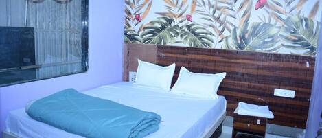 A bedroom with a bed, a nightstand, and a wall with a tropical leaf pattern.