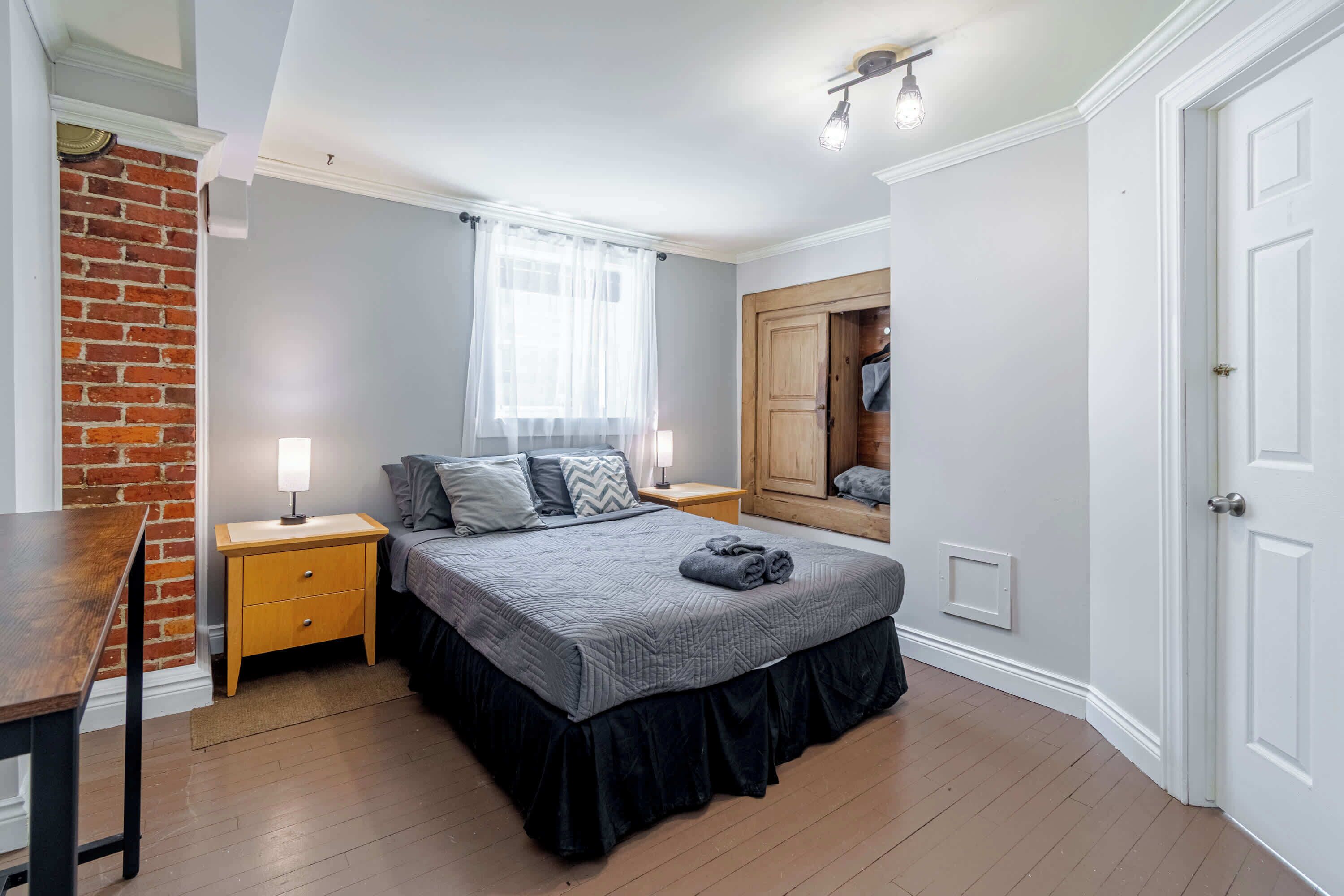 A bedroom with a bed, nightstands, a wooden dresser, a mirror, and a door.