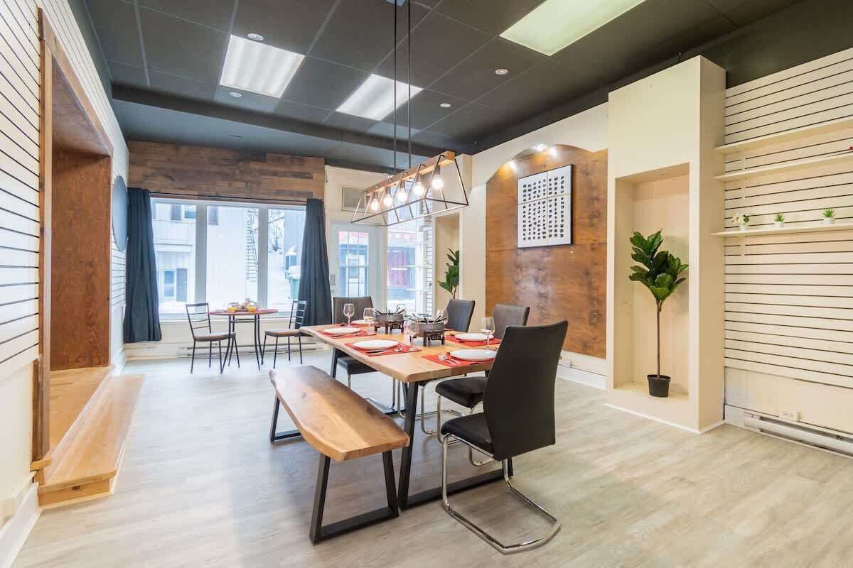 A modern dining area with a wooden table, black chairs, and a bench. There is a large window providing natural light and a view of the outside.