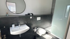 A modern bathroom with a white sink, a toilet, and a glass shower enclosure. - In & Out Boardinghouse Deluxe room (Stolberg)