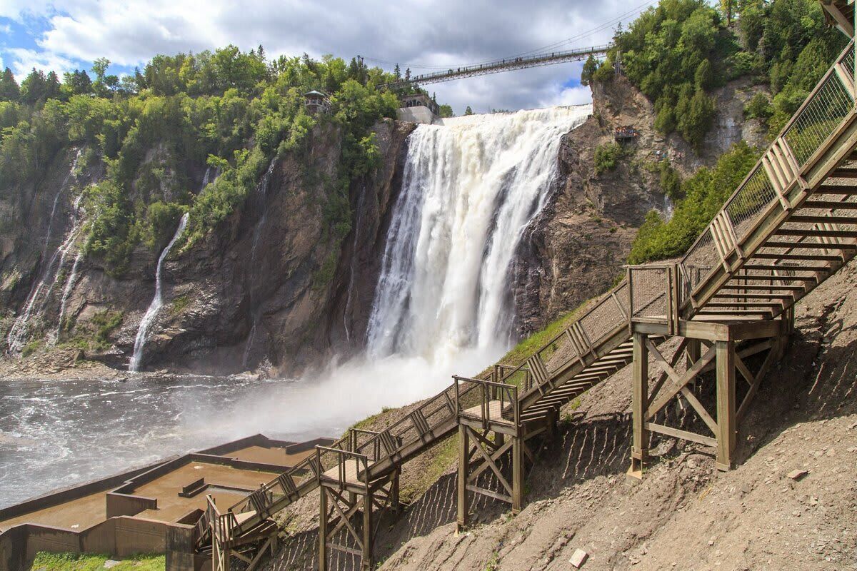 Una escalera de madera que lleva a una plataforma panorámica con vistas a una cascada.