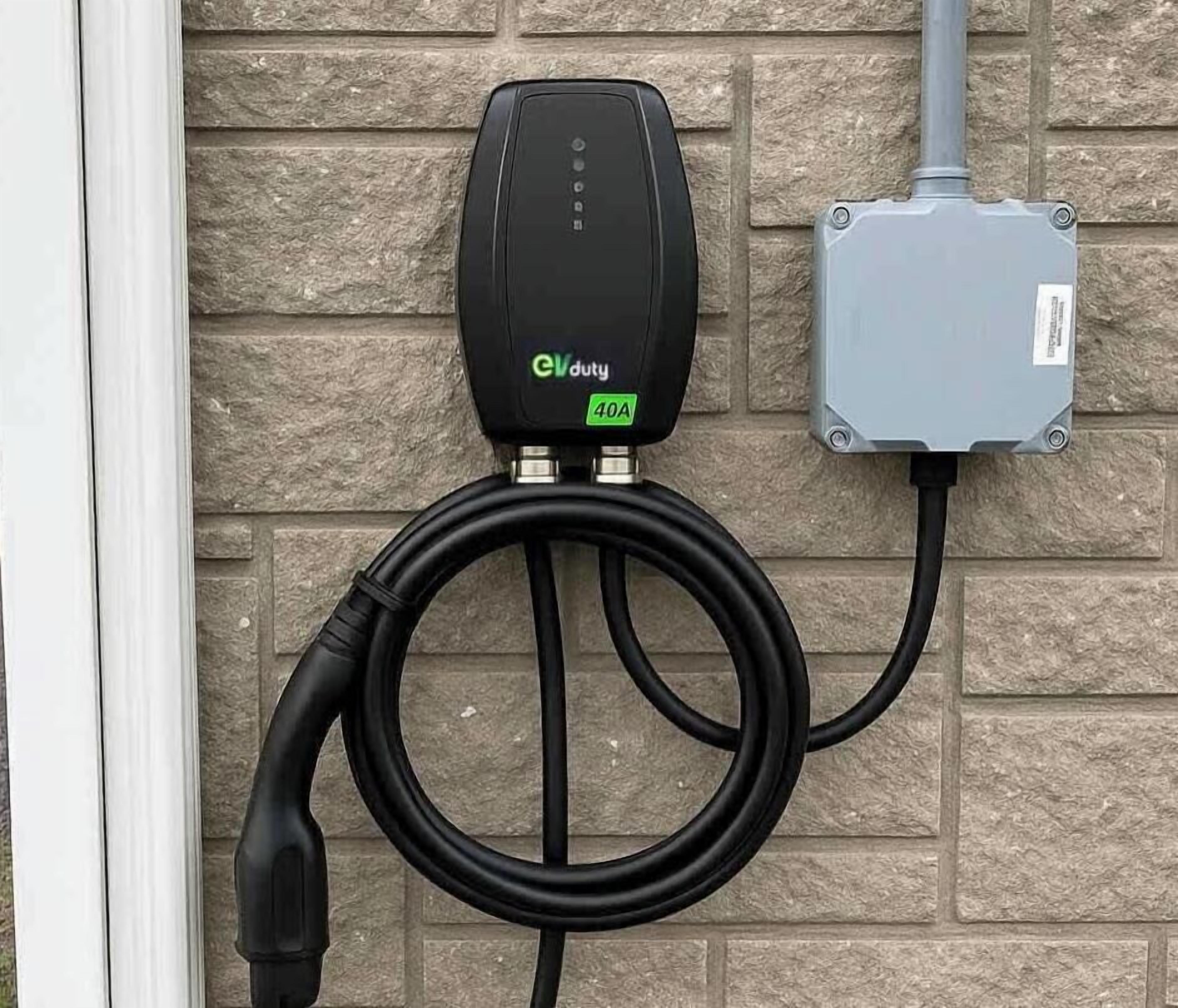 Une borne de recharge pour véhicules électriques, dotée d’un câble relié au mur extérieur d’un bâtiment.