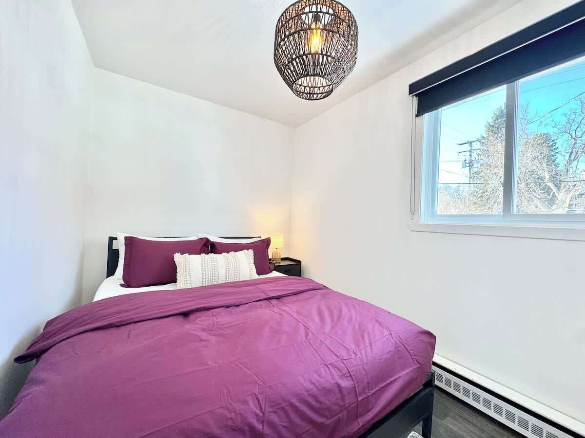 A bedroom with a bed, a nightstand, a lamp, and a window with a view of trees.