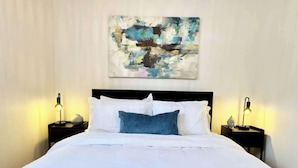 A neatly made bed with white linens and a single blue pillow, flanked by two bedside tables with lamps and decorative items.