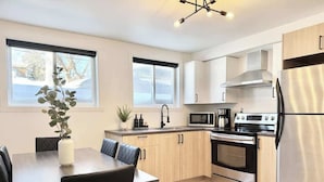 A modern kitchen with a dining area, stainless steel appliances, and light wood cabinetry.