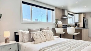 A modern bedroom with a large bed, bedside table, and a view of the kitchen. - Le Tulum – with EV Charger (Level 2) (Québec City)