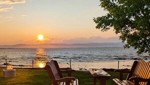 Vista do pôr do sol de um deck com duas cadeiras de madeira e uma mesa, com vista para a água.