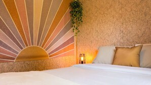 A hotel room with a bed, a wall with a sunburst design, a hanging plant, and a bedside lamp.