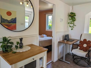A room with a bed, a desk with a laptop, a rocking chair, a mirror, and a hanging plant.