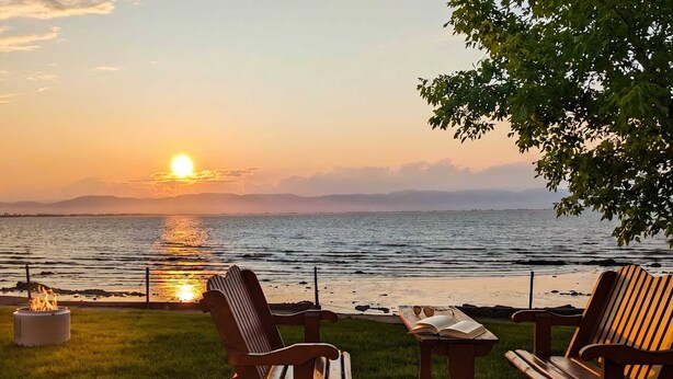 A sunset view from a deck with two wooden chairs and a table, overlooking a body of water.