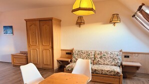 Ein gemütliches Zimmer mit einem Holztisch, zwei weißen Stühlen, einem floralen Sofa und einem Holzschrank.