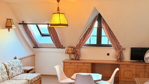 Ein gemütliches Zimmer mit einer Couch, Esstisch, Stühlen, einem Fernseher und einem Deckenventilator.