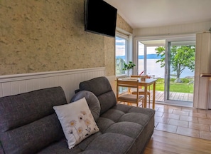 A living room with a sofa, a flat-screen TV, a dining table with chairs, and a view of the outdoors.