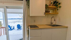 A compact kitchen with a built-in sink, a small countertop, and a sliding door leading to a balcony with blue chairs.