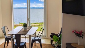 A dining area with a table and chairs, a TV mounted on the wall, and a view of a body of water through large windows.