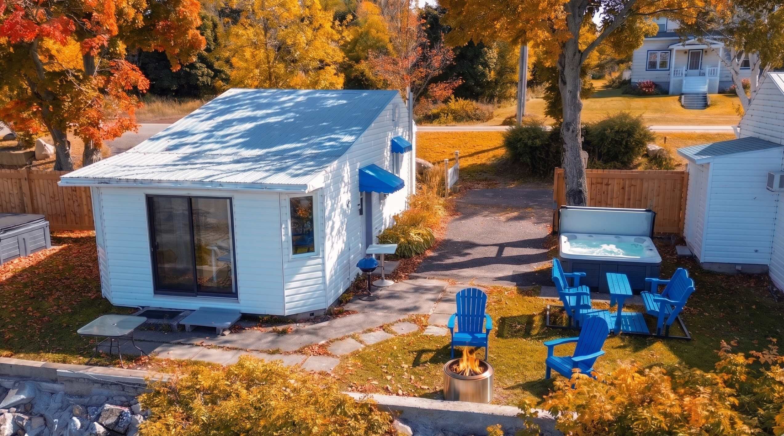 A small white cabin with a glass door, a fire pit, and blue Adirondack chairs.
