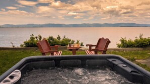 Un bain à remous avec deux fauteuils donnant sur un lac et des montagnes en arrière-plan.