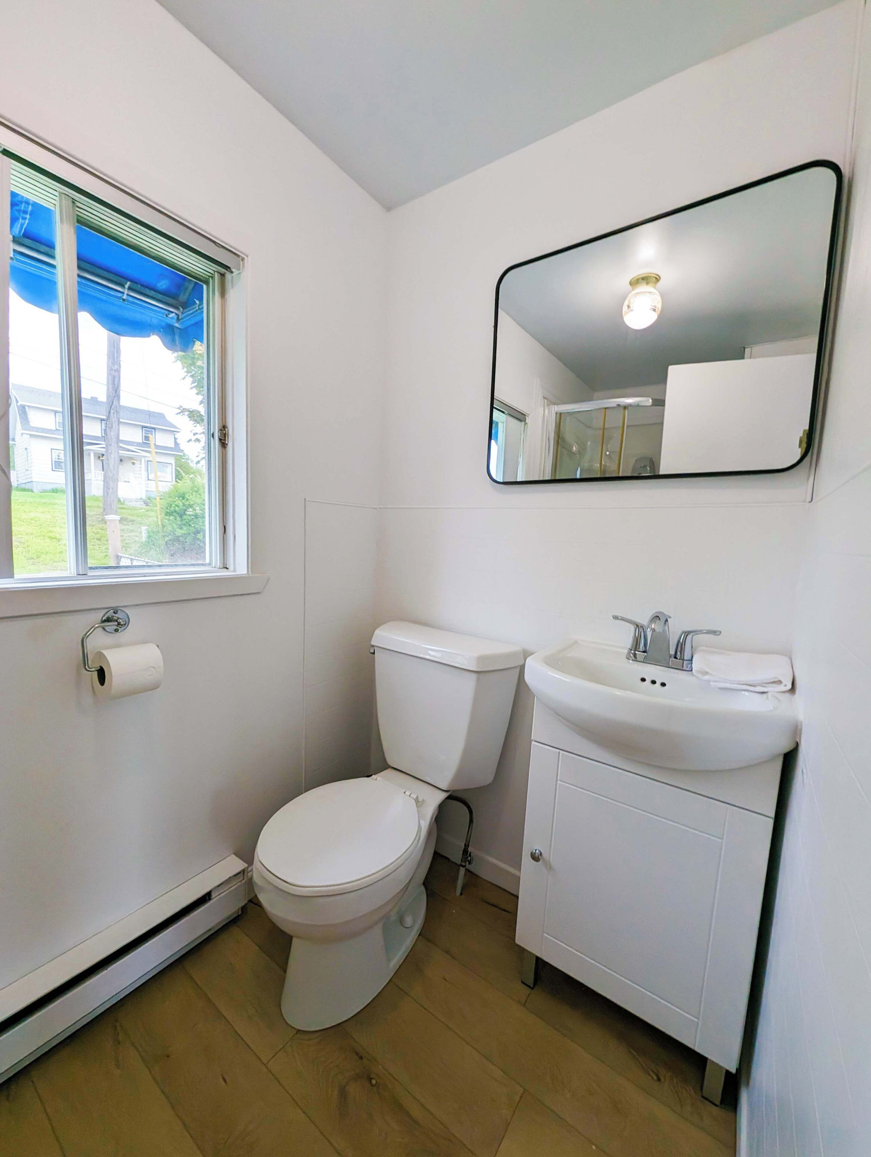 A small, clean bathroom with a toilet, sink, and mirror.