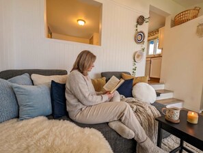 A person sitting on a sofa with a book, a mug, and a candle on a small table.