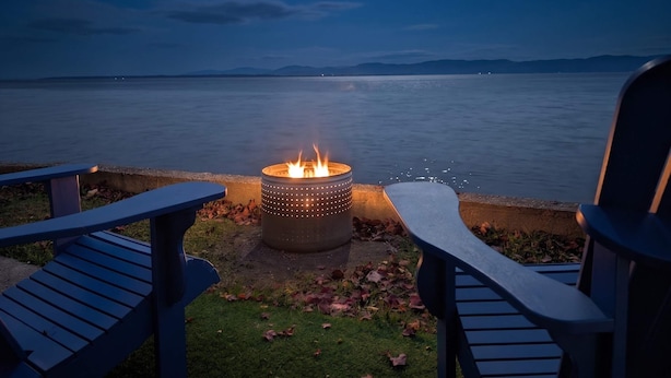A fire pit with a view of a calm body of water and distant mountains. - Chalet Studio #6 Waterfront with Spa, Fireplace & Wifi (Cap-Saint-Ignace)