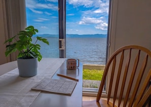 Una mesa con una planta, una taza y un tablero de juego junto a una ventana que da al mar.