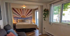 Une chambre Ă coucher avec un lit, une table de chevet, une plante suspendue et une fenĂȘtre donnant sur un beau paysage.